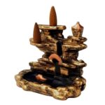 Este é um incensário de resina, projetado para parecer uma cascata dourada com detalhes em cobre. Possui dois suportes para cones de incenso em diferentes níveis. A estrutura imita uma formação rochosa, e há um pequeno recipiente na base para coletar as cinzas do incenso. Este incensário é perfeito para adicionar um toque decorativo e criar um ambiente relaxante. Especificações: – Porta Incenso – Material: Resina. Dimensões (A x L x P): – 13 x 14 x 8 cm.